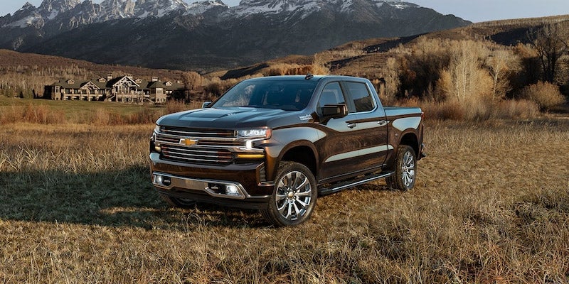 A Chevy Silverado 1500 parked out in a country field in front of the snow capped mountains