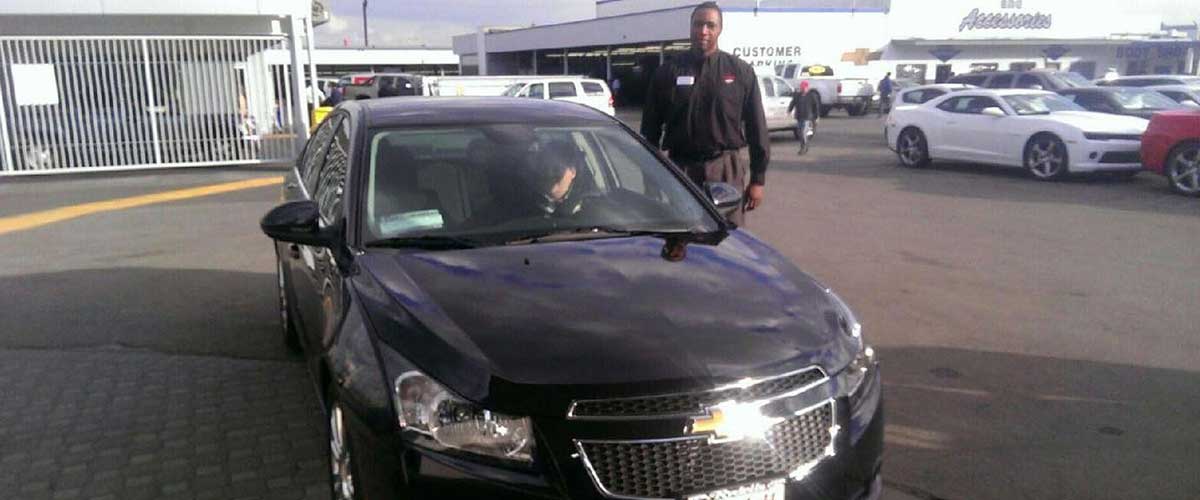 A salesman and customer posed by a black Chevy car