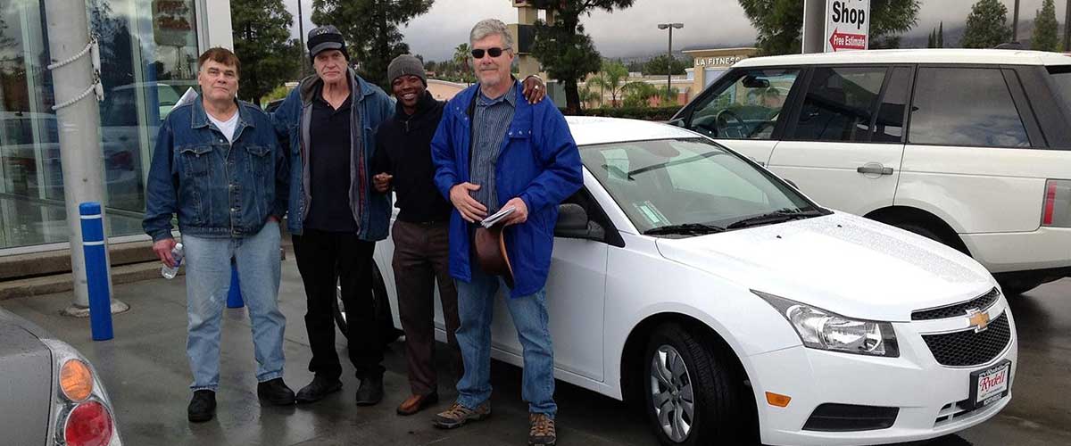 A salesman and three men posed in front of a white Chevy car