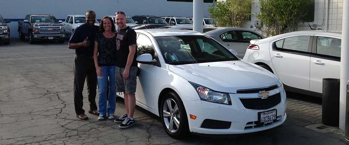 Two customers and their salesman posed in front of their new car