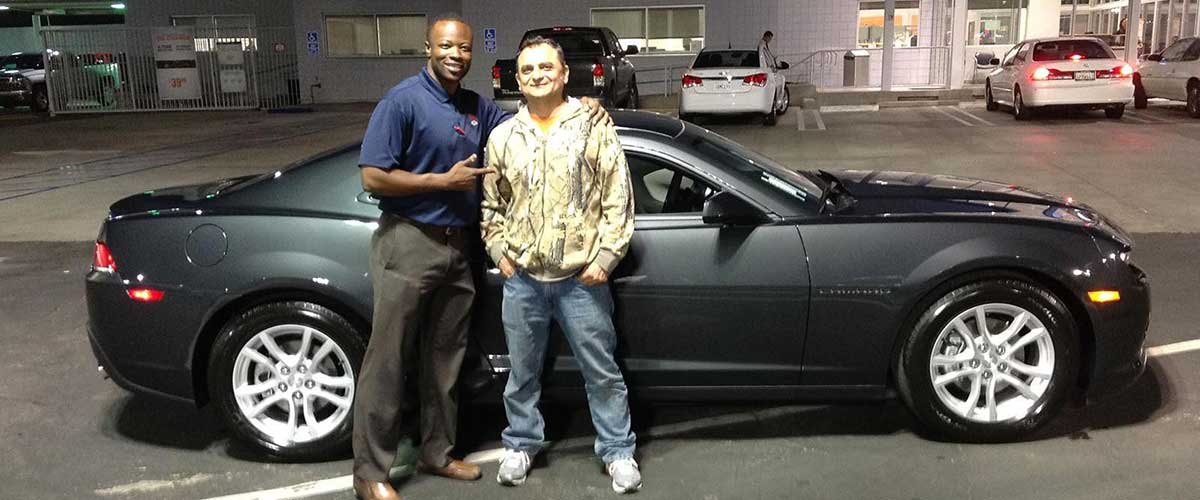 A customer and salesman posed in front of a black Chevy Corvette